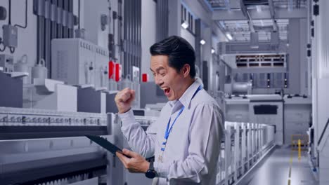 side view of an asian male professional worker standing with his tablet at pharmaceutical factory, vaccine production facility, he raises his fist up with screaming goal after check on the tablet