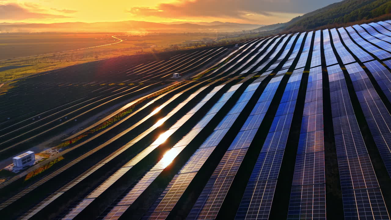 Aerial view of a solar power station during sunset, featuring sun flares reflecting off the photovoltaic panels. Solar power plant at sunset
