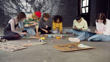 young environmental activists painting placards sitting on the floor