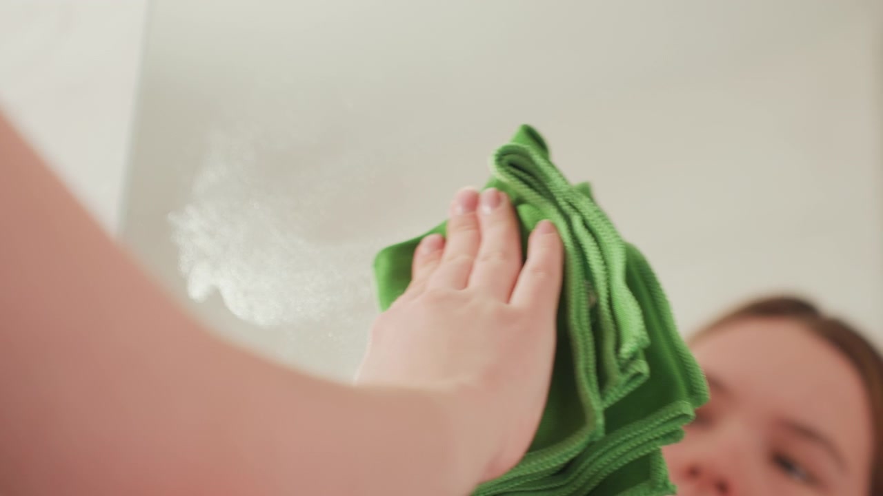 Primo piano di una mano che pulisce uno specchio con un panno verde