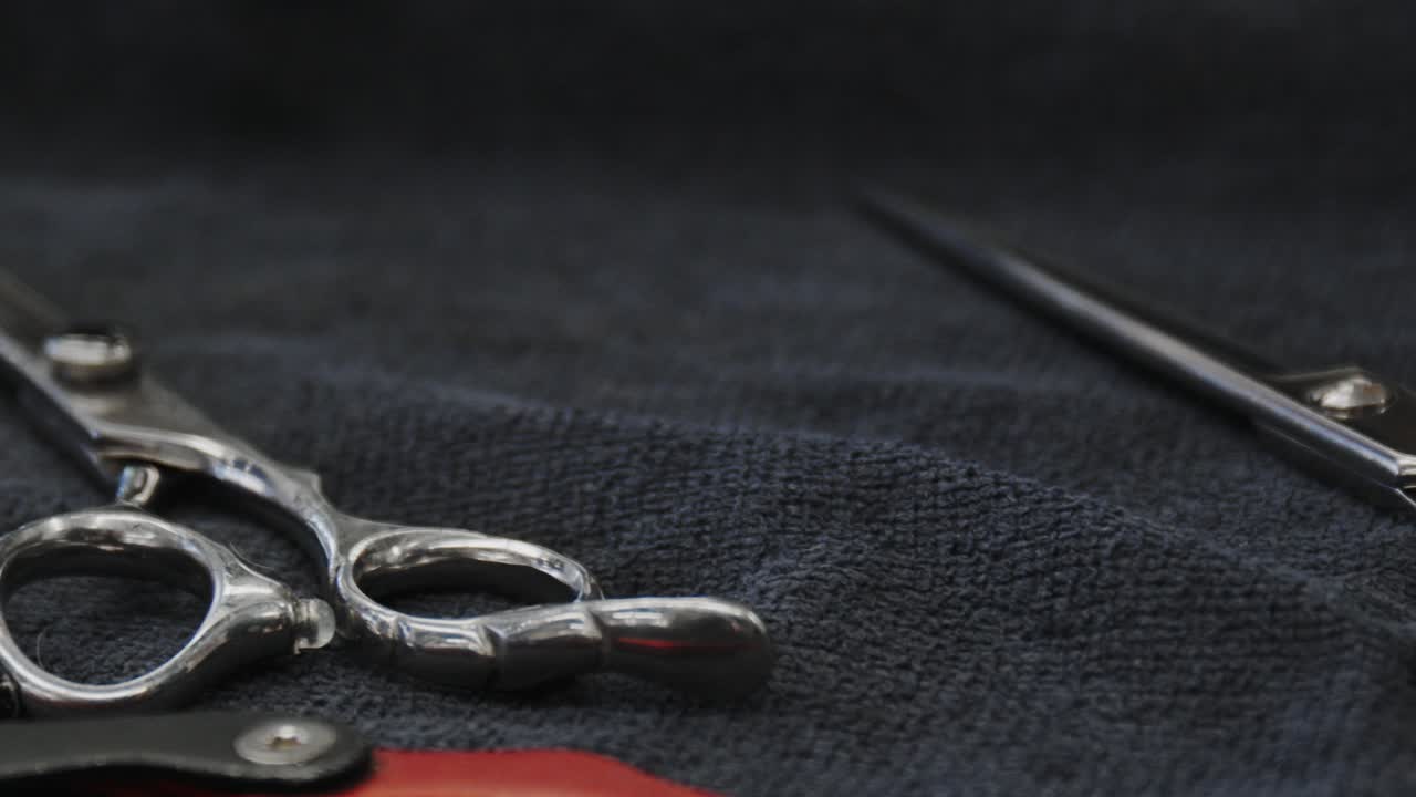 Multiple scissors played out on a cloth and a mans hand comes in and grabs a pair of hair cutting scissors