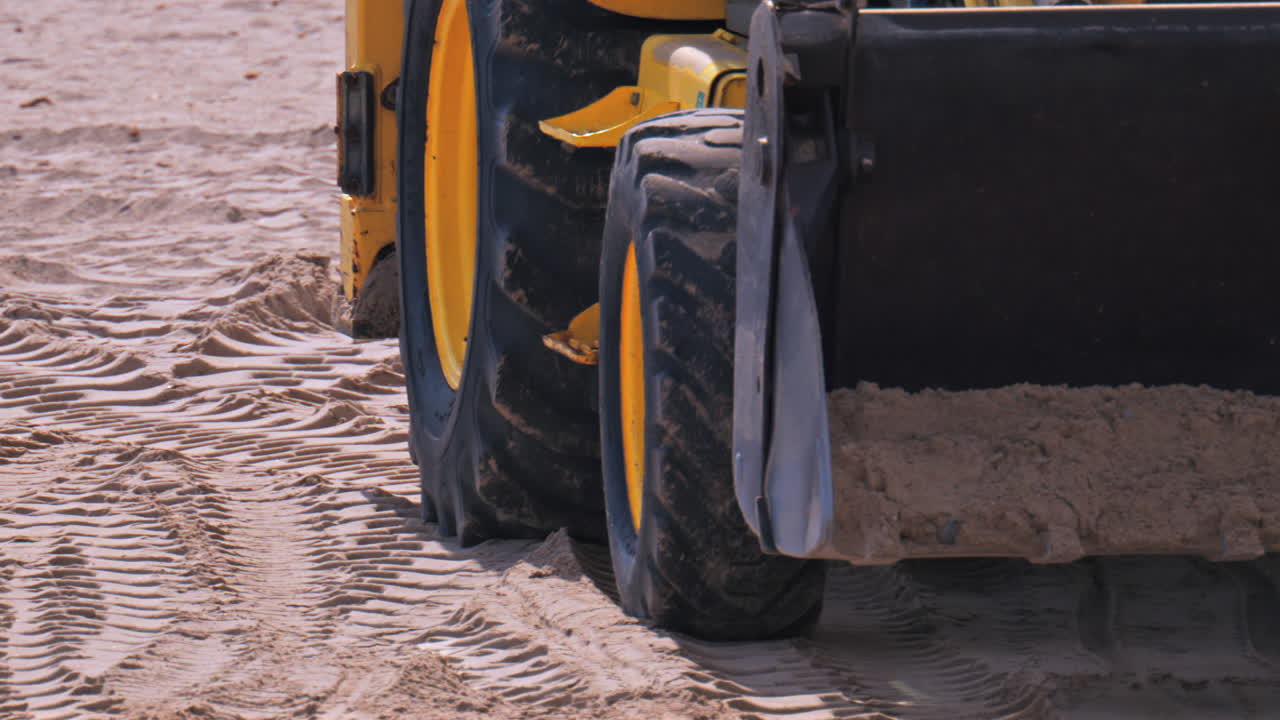 Close up of the wheels of an yellow loader moving on the sandy beach