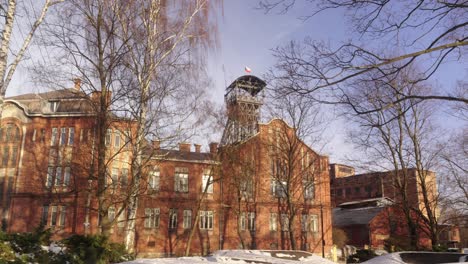 old brick building with a minning tower, surrounded by bare trees under a clear sky