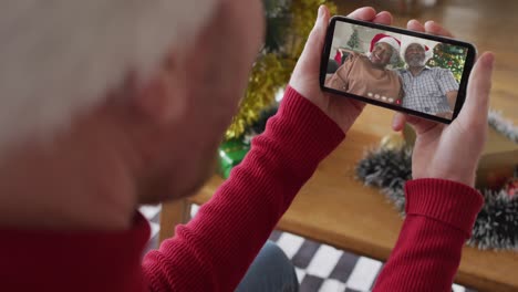hombre caucásico usando un teléfono inteligente para una videollamada de navidad, con una familia sonriente en la pantalla