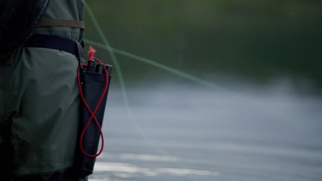 Fly-fishing-line-moves-in-front-of-unrecognizable-man-by-blurry-water