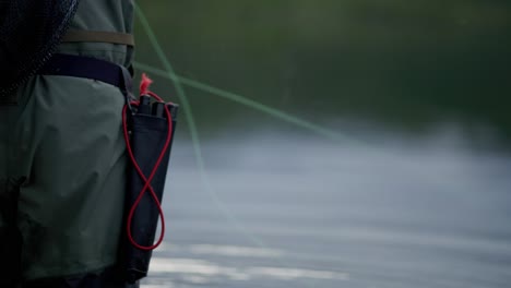 fly fishing line moves in front of unrecognizable man by blurry water