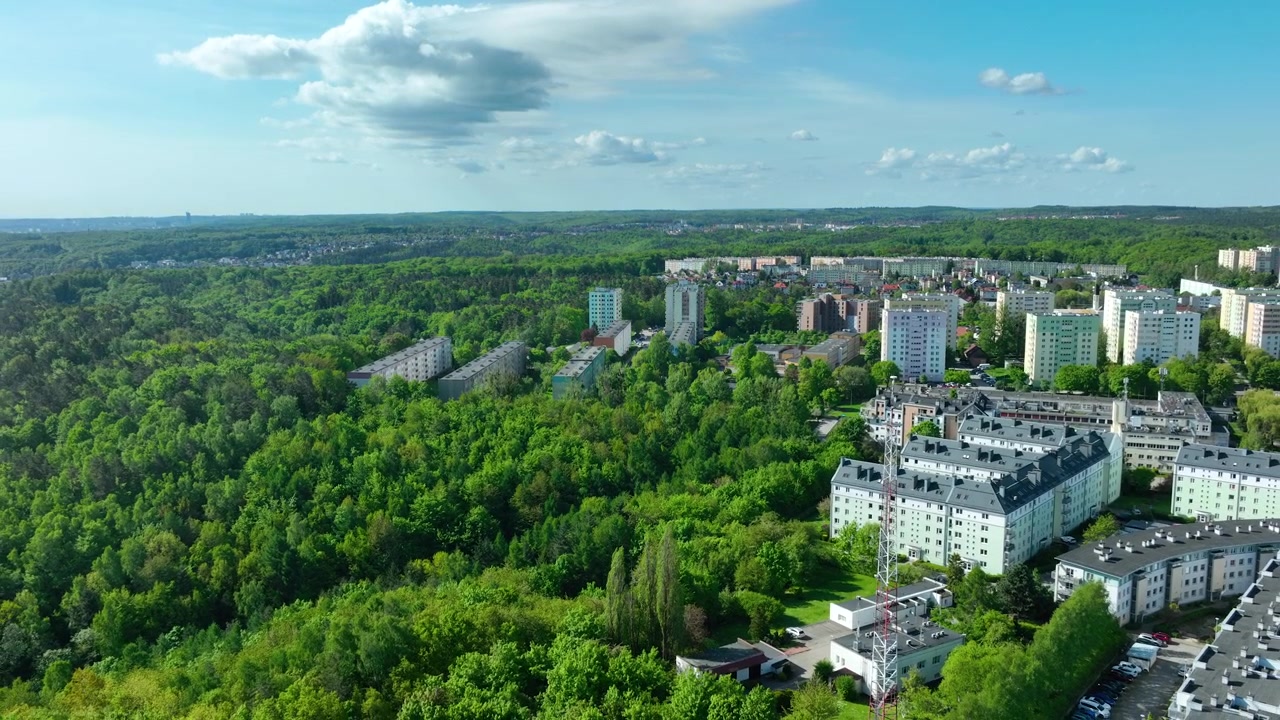 Tomada aérea cinematográfica de edifícios de apartamentos residenciais em Gdynia, Polônia, perfeitamente integrados com florestas verdes exuberantes sob um céu azul. Adequado para temas de planejamento urbano e sustentabilidade
