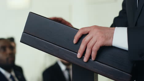 close-up view of caucasian male hands on a podium and gesticulating while businesswoman is making a speech to the audience at a conference