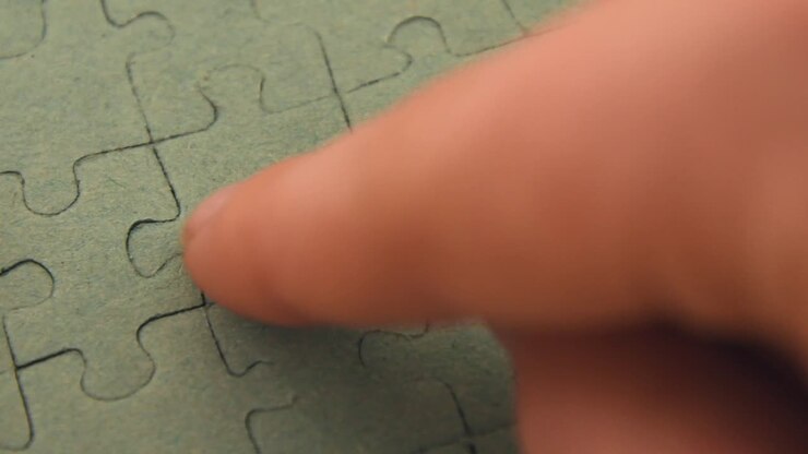 Primo piano della mano di una bambina che inserisce un pezzo di puzzle nell'ultimo spazio vuoto, completando un puzzle a tinta unita, su uno sfondo di legno chiaro.
