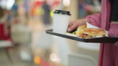 close up of a woman in pink dress carrying lunch tray with burger, fries, and drink, walking toward her table, she adjusts the tray on the table, with light reflection seen on the tray