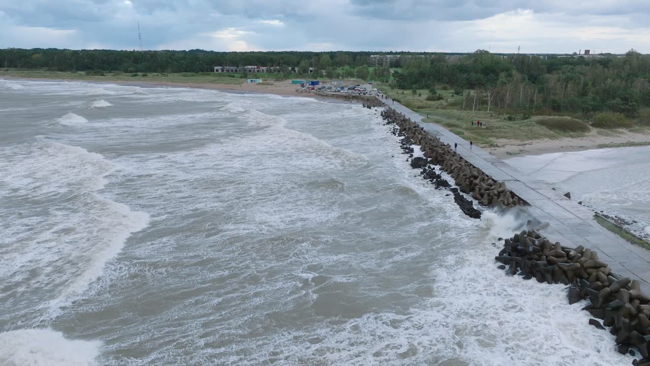 vista aérea del muelle de hormigón del puerto de liepaja, tormenta de otoño, grandes olas salpicando, día nublado, amplia toma de avión no tripulado avanzando