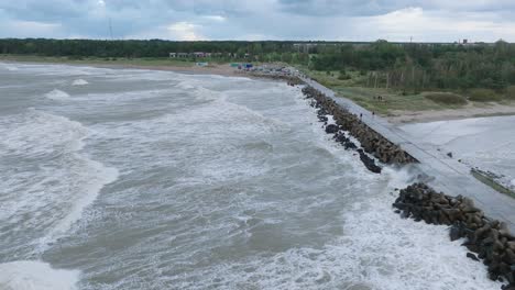 aerial establishing view of port of liepaja concrete pier , autumn storm, big waves splashing, overcast day, wide drone shot moving forward