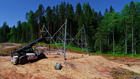 aerial rotation revealing professional worker installing high voltage tower in forest firebreak