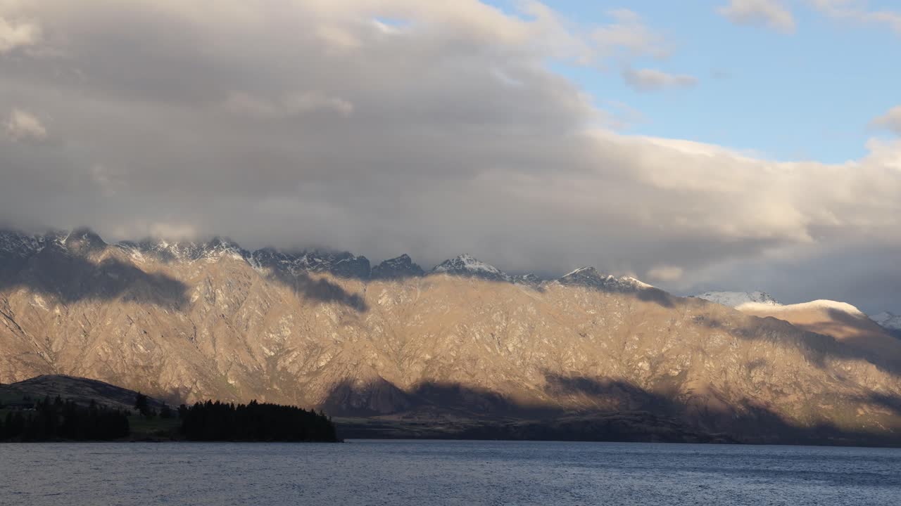 Clouds drift over mountains and a lake in Glenorchy, New Zealand, creating dynamic lighting and shadows in a serene landscape