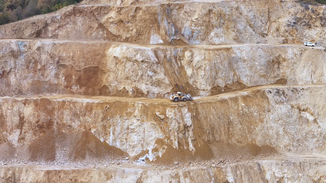 An Excavator Operating on a Terraced Mining Site, Digging Through Layers of Rocky Earth to Extract Minerals - Zoom In Shot