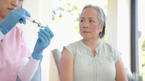 nurse preparing syringe for vaccination while senior asian woman waiting attentively