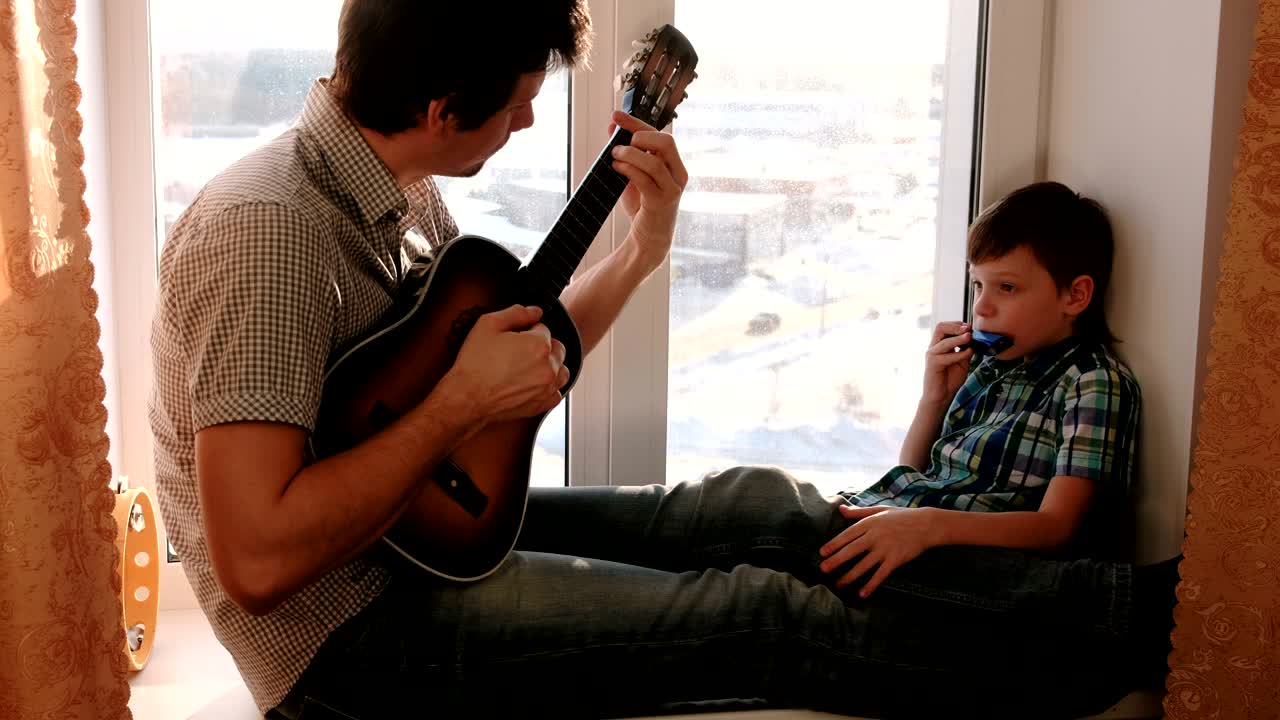 음악 악기: 아빠가 기타를 연주하고, 아들은 창문 앞에 앉아서 오르간을 연주하고 있다.