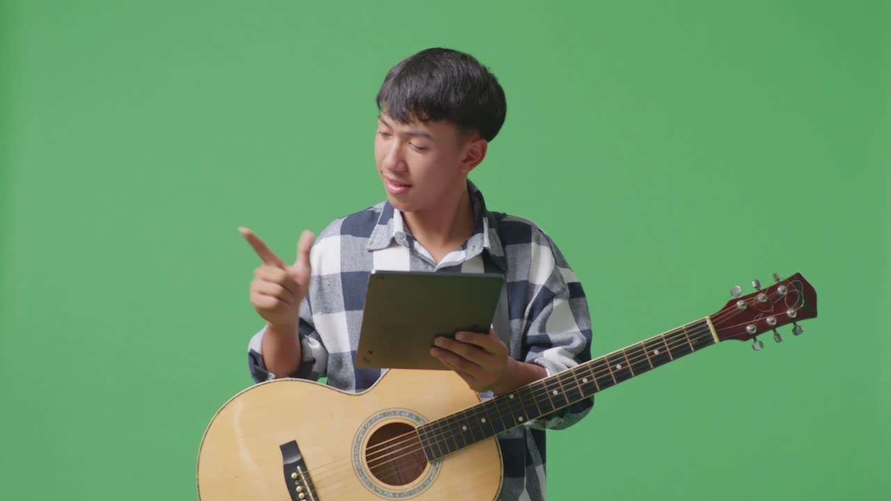 초록색 스크린 배경 에 서 있는 동안 태블릿 을 들고  을 가리키는 기타 를 들고 있는 아시아 청소년