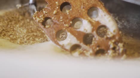 brewing handcraft beer - mixing malted grains with water in the brewing tank using a wooden spoon with holes - extreme close up slowmo