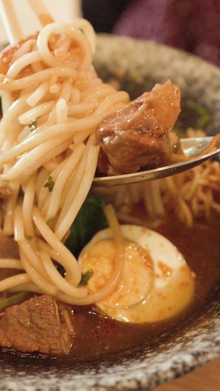 Primo piano di manzo e noodles sollevati da una ciotola di zuppa birmana piccante a Bangkok.