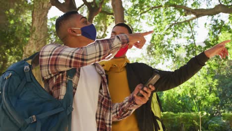 Two-happy-mixed-race-male-friends-using-smartphone-in-park-with-backpacks