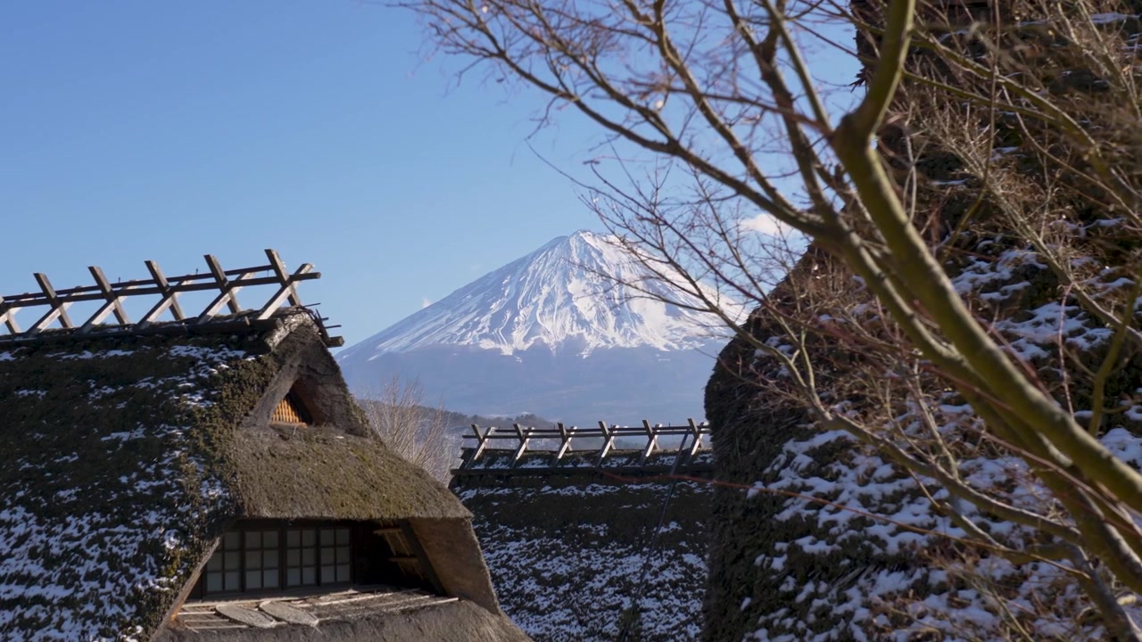 Paisagem em câmera lenta de casas com telhados de colmo nevados em uma vila tradicional japonesa, com o pico do Monte Fuji ao fundo, perto do Lago Saiko em Kawaguchiko, Yamanashi, Japão, turismo e atividades ao ar livre.