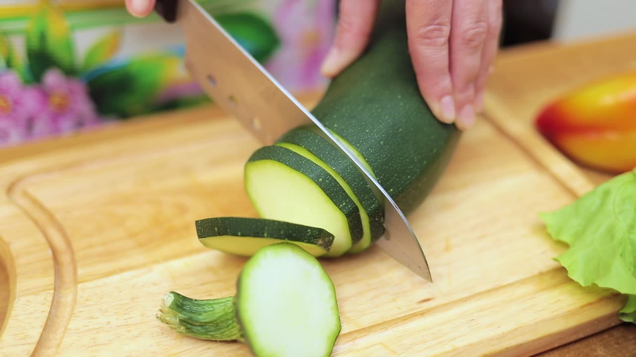 Women's hands Housewives cut with a knife fresh zucchini on the cutting Board of the kitchen table