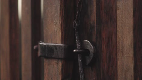 close-up of a hand closing an old wooden gate with a metal latch on a chain