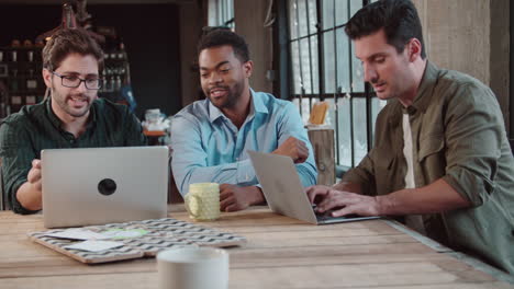 three male designers in meeting using laptops