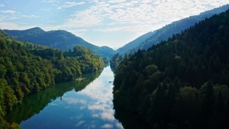 Crystal-clear-blue-reflecting-river-between-clad-mountains-in-an-idyllic-landscape-bathed-in-sunlight