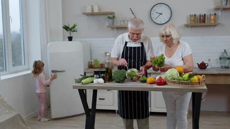 Ältere-Großmutter-Und-Großvater-Kochen-Salat.-Enkelin-Gibt-Gemüse-Aus-Dem-Kühlschrank