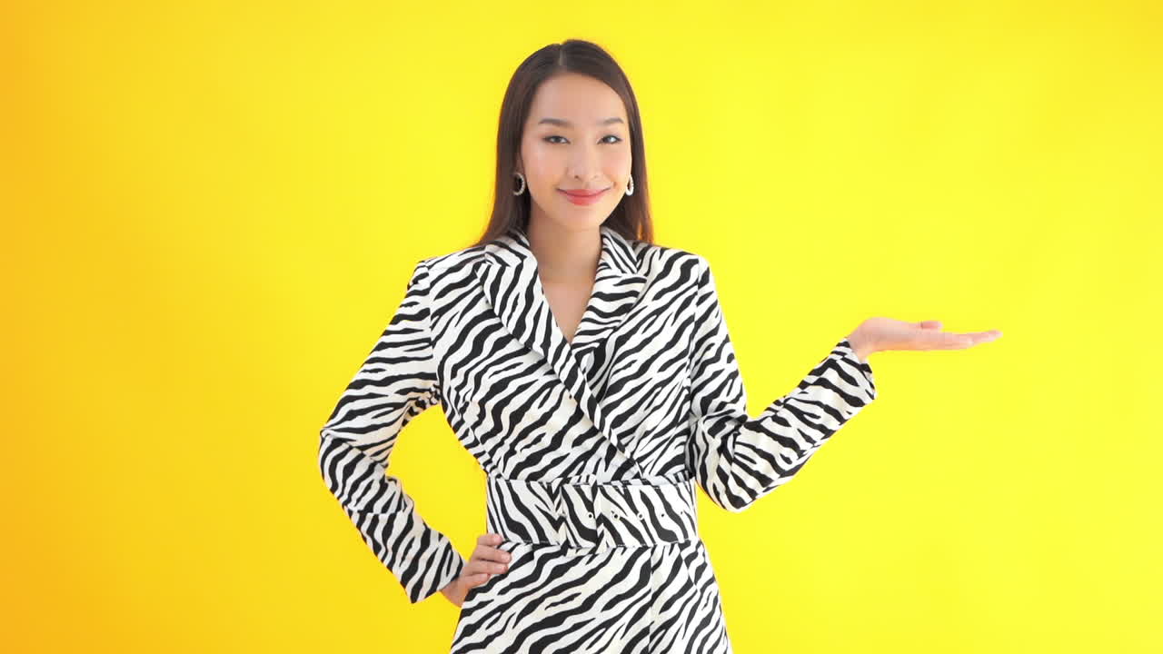 A stylish young woman places her hand on her hip and uses a flat palm to display a product to copy space on her left