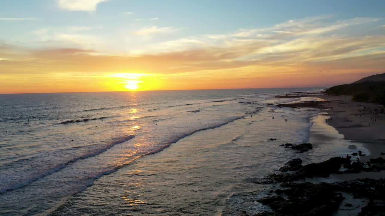 antena de impresionante puesta de sol reflejada en el agua con olas y surfistas en el océano pacífico en tamarindo, costa rica