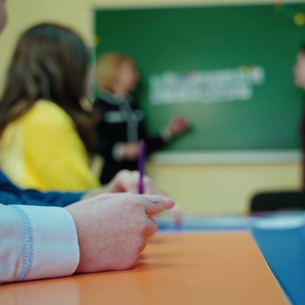 Blurred classroom background. Students sitting in class and teacher talking to a teen school child near the blackboard at school. Education concept.