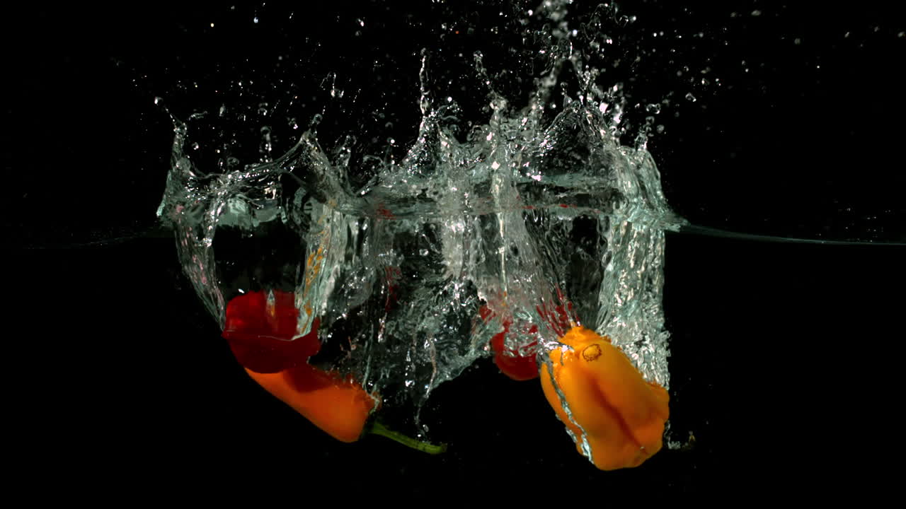pimientos de chile cayendo en el agua sobre un fondo negro