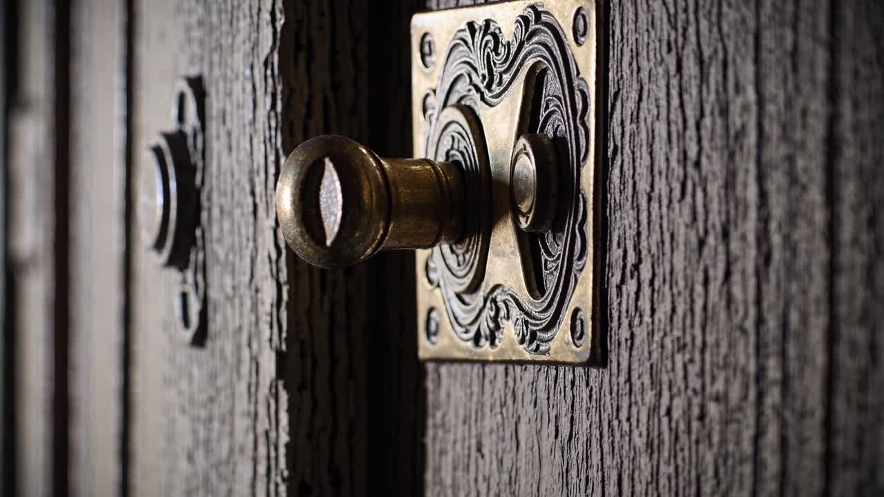 Video ravvicinato di un pomello in ottone ornato su una porta di legno con trama, ripreso da un'angolazione laterale.