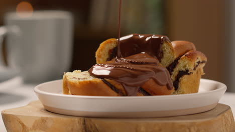 nahaufnahme von geschmolzener schokoladensauce, die auf ein schokoladen-babka-brötchen auf teller 1 gegossen wird