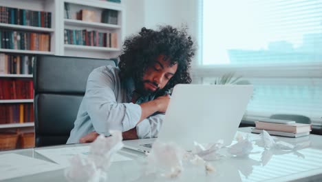 young arabian man yawns and rests head on table next to laptop and falls asleep