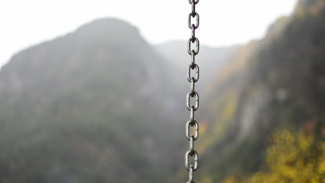 a chain from a swing chair dancing in the rain during a cold autumn day, the blurry mountains behind offer a beautiful scene