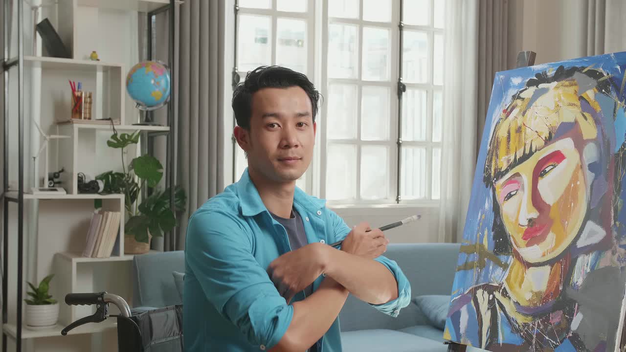 Asian Artist Man In Wheelchair Holding Paintbrush Mixed Colour Turn To Cross His Arms And Smile While Painting A Girl On The Canvas
