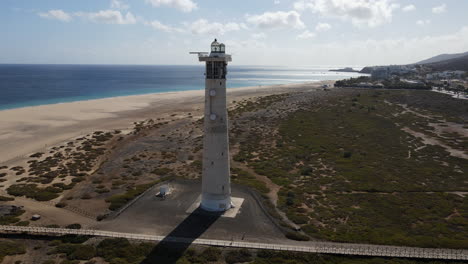 toma aerea en orbita ya media distancia del faro de morro jable, con la playa de morro jable al fondo