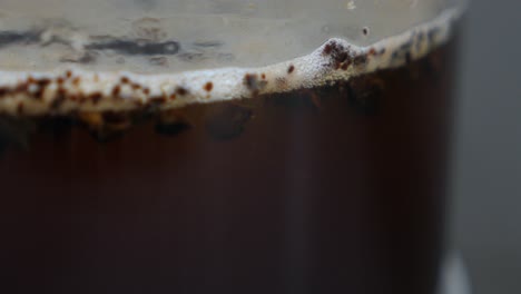 Side-view-of-large-coffee-granules-falling-in-liquid-in-french-press-plunger,-slow-motion-macro-close-up