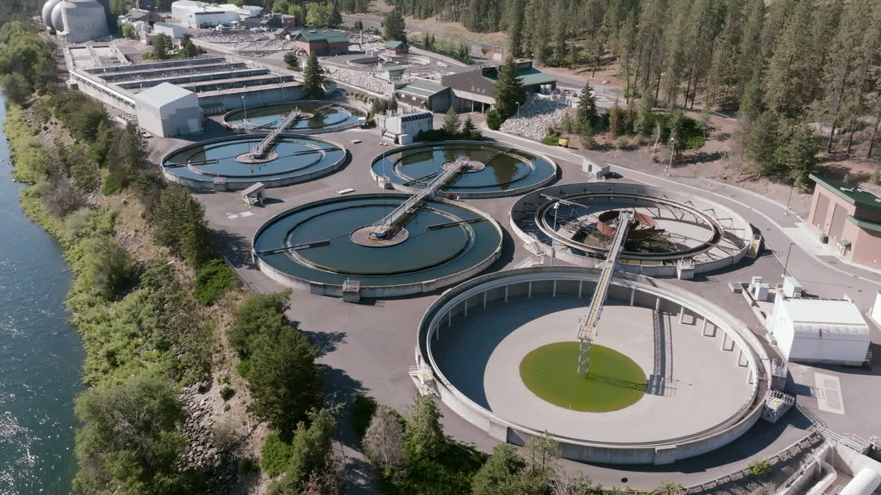 Multiple circular clarifier tanks sit beside the river in a visually striking arrangement, highlighting the industrial design and layout of the facility