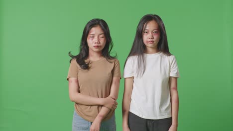 young asian women victims of violence with bruise on bodies hold their arms looking into camera sadly in the green screen background studio