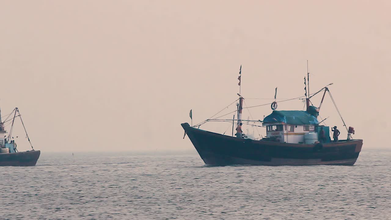 Two Small fisherman boat sailing in middle of the ocean with fisherman preparing to dock during sunset with small calm waves and returning home in foggy weather video background in mov in full HD
