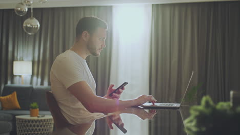 man working on laptop and smartphone at home