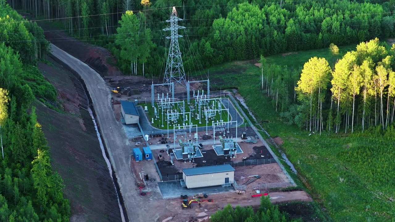 Aerial view of a new electrical substation with a power line tower in a remote wooded area