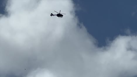 slo mo of helicopter flying into frame from top left overhead with puffy clouds behind and blue sky and exits frame left