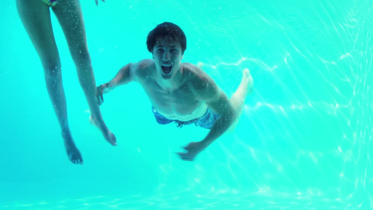 Coppia felice che salta in piscina salutando la telecamera