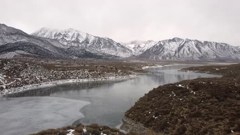 panoramic aerial view of crowley lake in cold winter california, vast wild snowy valley, lake shore lands and snow covered rocky mountains in horizon